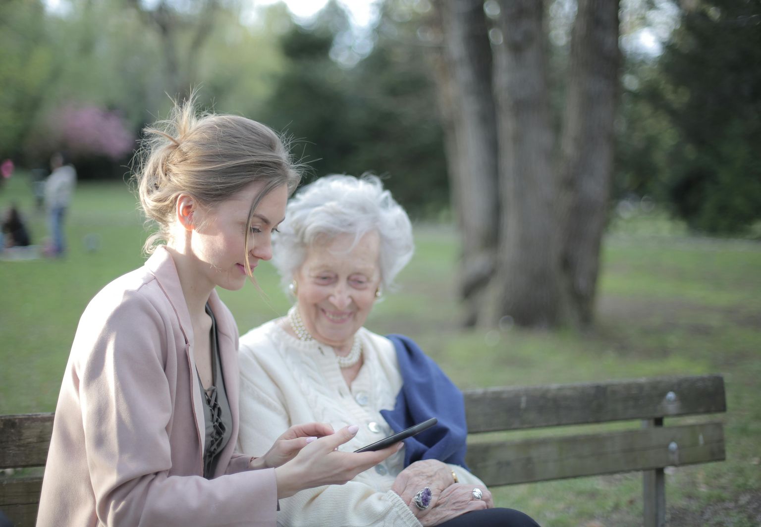 smiling elderly woman looking at young woman's iphone